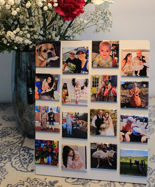 Custom photo magnets of family, pets, a wedding and a new baby on a white magnetic board beside a vase of flowers